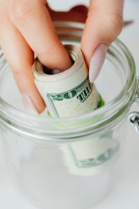 Services Hand placing rolled US dollars into a glass jar, representing savings and financial planning.